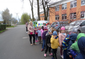 Dzieci maszerują pod budynkiem szkoły podstawowej z transparentami ekologicznymi.